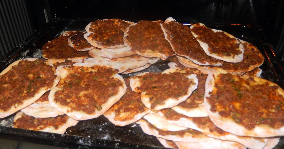 Freshly baked Armenian lahmajoun — thin crispy flatbread topped with spiced minced meat, diced tomatoes, and fresh parsley, ready to be rolled with lemon
