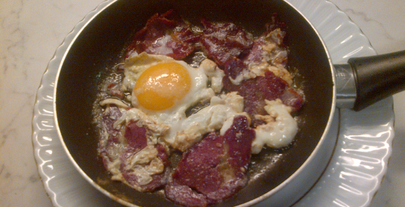 Armenian basturma and eggs — thinly sliced spiced cured beef sizzling in a pan with scrambled eggs, served alongside fresh tomatoes and lavash for a classic Armenian breakfast