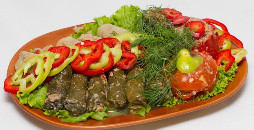 A platter of Armenian dolma — tender grape leaves tightly stuffed with herb-seasoned rice and ground lamb, served with yogurt and lemon wedges