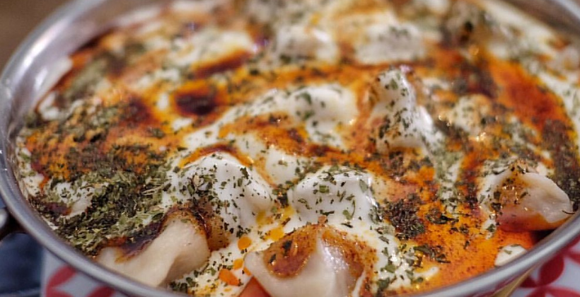Armenian manti — tiny boat-shaped baked lamb dumplings arranged in a dish, topped with garlic yogurt, paprika butter, and fresh mint