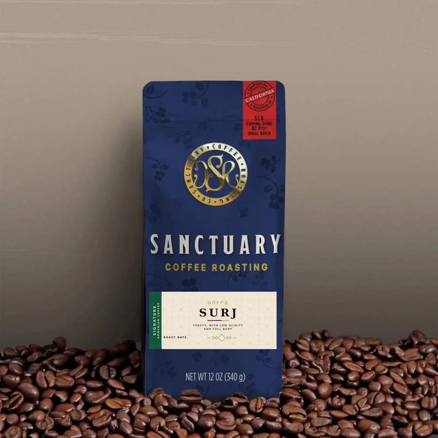 A 12 oz bag of Surj Armenian coffee from Sanctuary Coffee Roasting Company, standing in roasted coffee beans