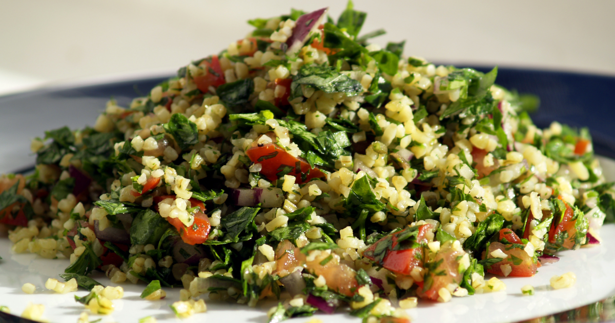 Fresh Armenian tabouleh salad with vibrant green parsley, red tomatoes, and bulgur wheat in a white serving bowl with lemon wedges